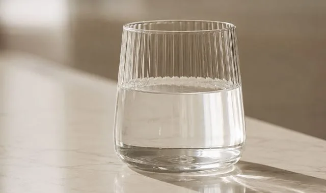 Un vaso acanalado de Kangen Water® transparente sobre una encimera iluminada por el sol